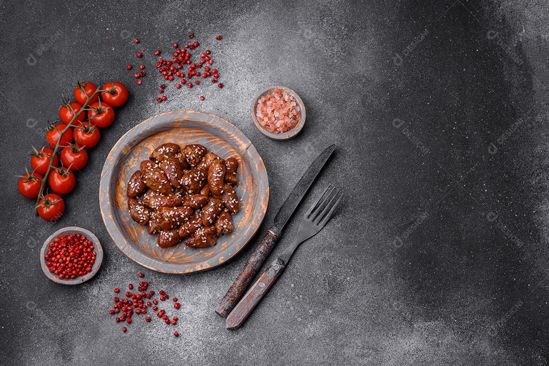 Corações de frango fritos em molho de soja com sal e especiarias em um prato sobre um fundo de concreto texturizado