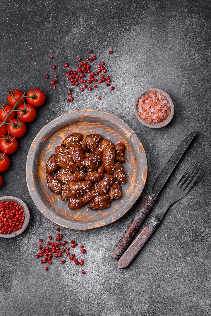 Corações de frango fritos em molho de soja com sal e especiarias em um prato sobre um fundo de concreto texturizado