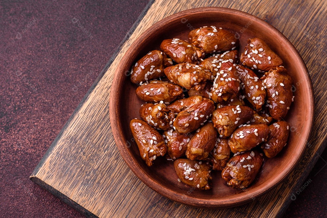 Corações de frango fritos em molho de soja com sal e especiarias em um prato sobre um fundo de concreto texturizado