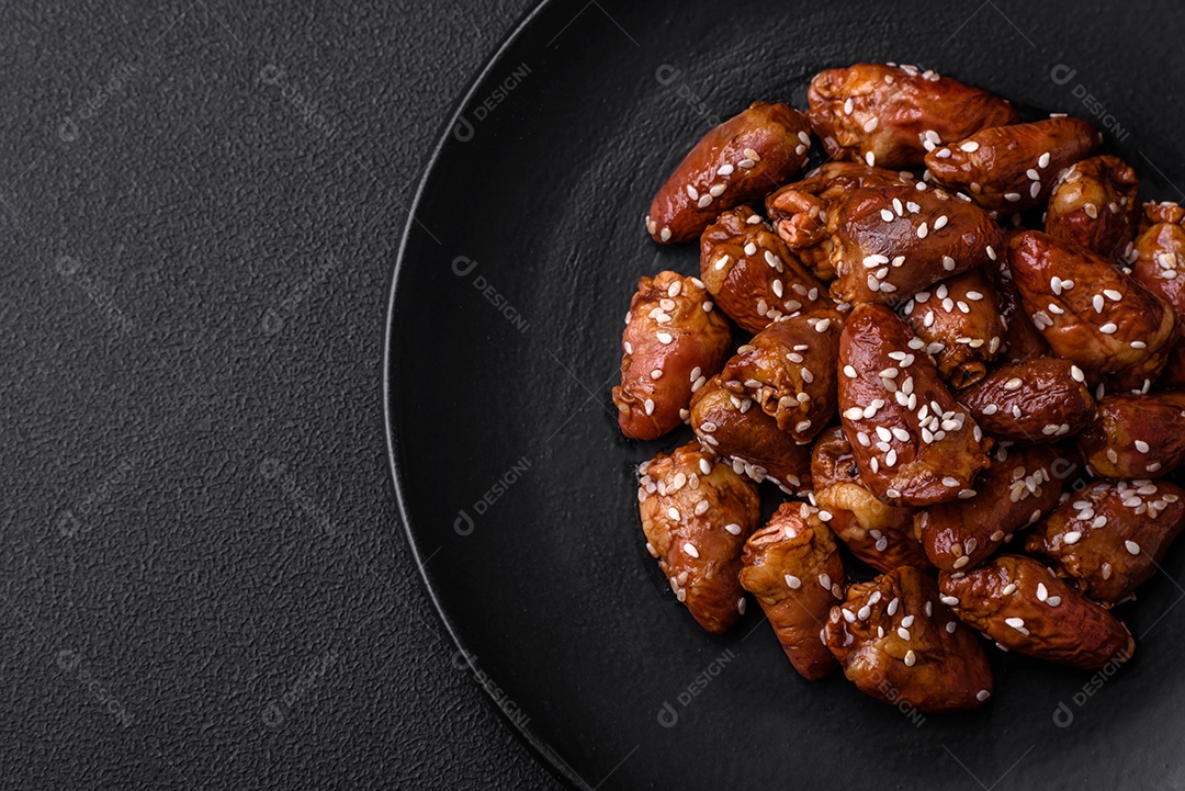 Corações de frango fritos em molho de soja com sal e especiarias em um prato sobre um fundo de concreto texturizado