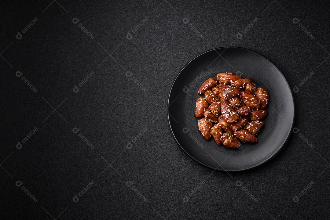 Corações de frango fritos em molho de soja com sal e especiarias em um prato sobre um fundo de concreto texturizado