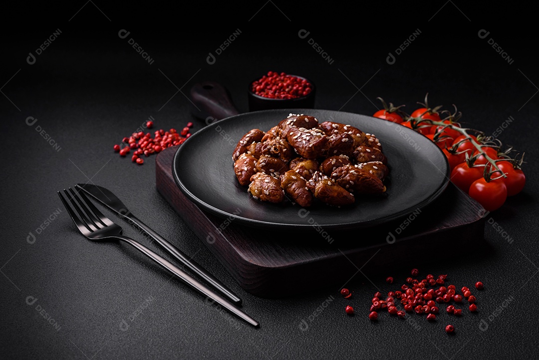 Corações de frango fritos em molho de soja com sal e especiarias em um prato sobre um fundo de concreto texturizado