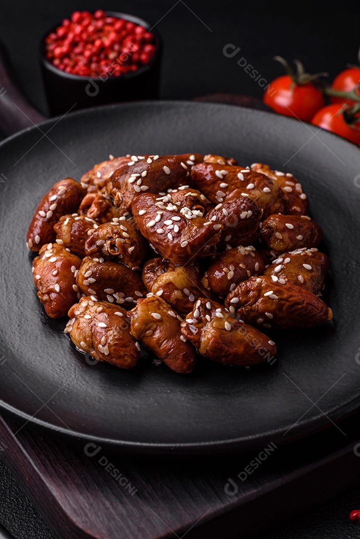 Corações de frango fritos em molho de soja com sal e especiarias em um prato sobre um fundo de concreto texturizado