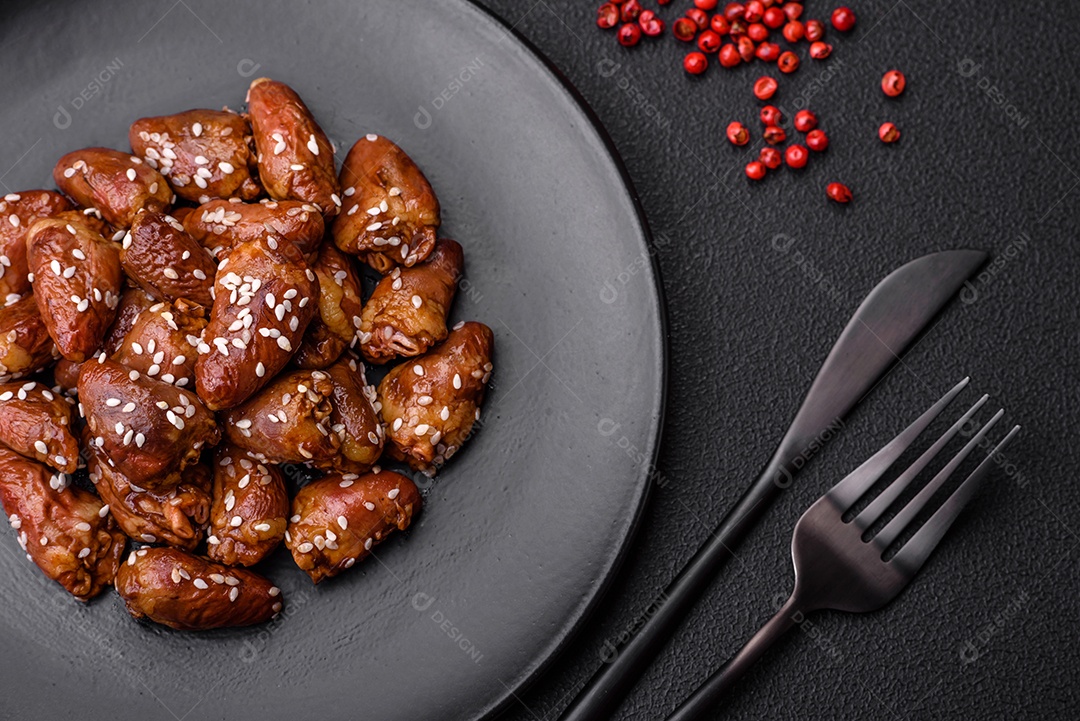 Corações de frango fritos em molho de soja com sal e especiarias em um prato sobre um fundo de concreto texturizado