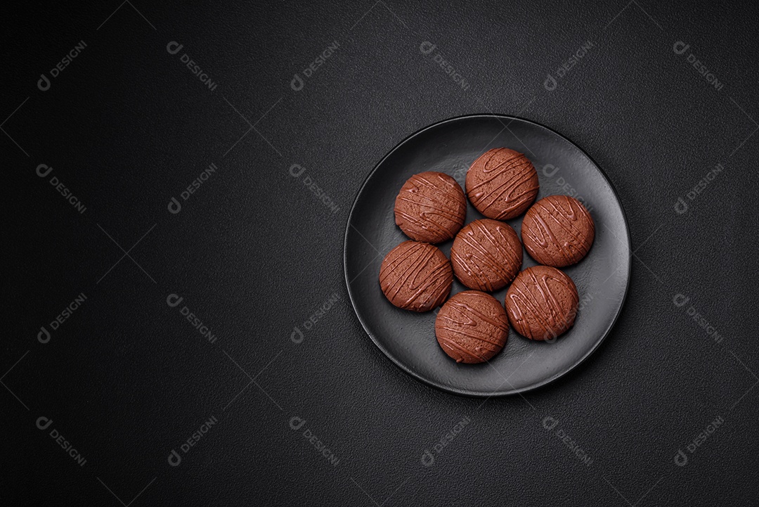 Deliciosos biscoitos de chocolate doce em uma placa de cerâmica preta sobre um fundo escuro de concreto