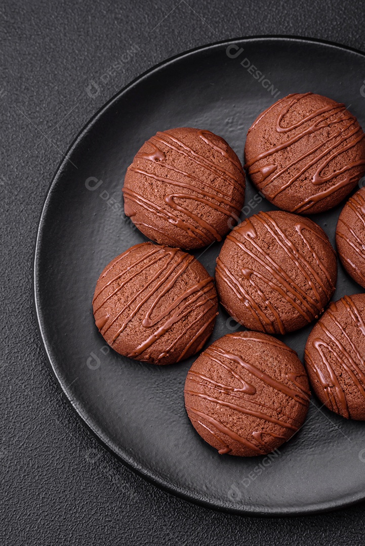 Deliciosos biscoitos de chocolate doce em uma placa de cerâmica preta sobre um fundo escuro de concreto