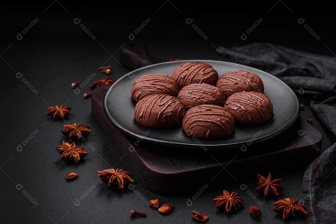 Deliciosos biscoitos de chocolate doce em uma placa de cerâmica preta sobre um fundo escuro de concreto
