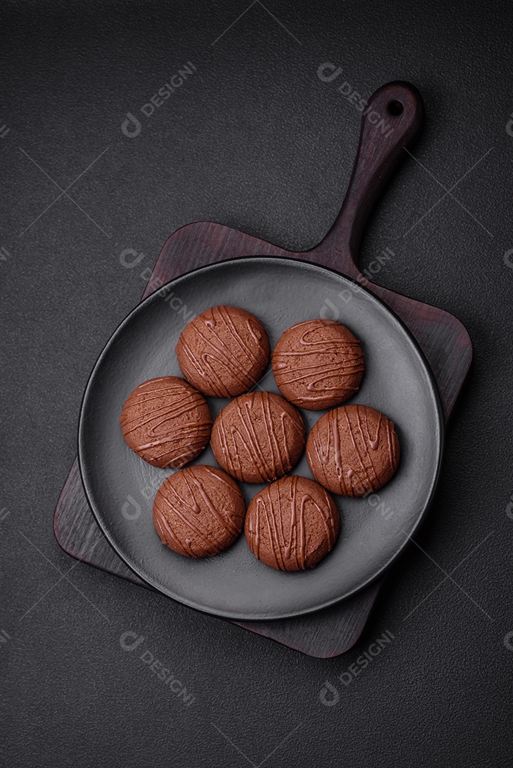 Deliciosos biscoitos de chocolate doce em uma placa de cerâmica preta sobre um fundo escuro de concreto