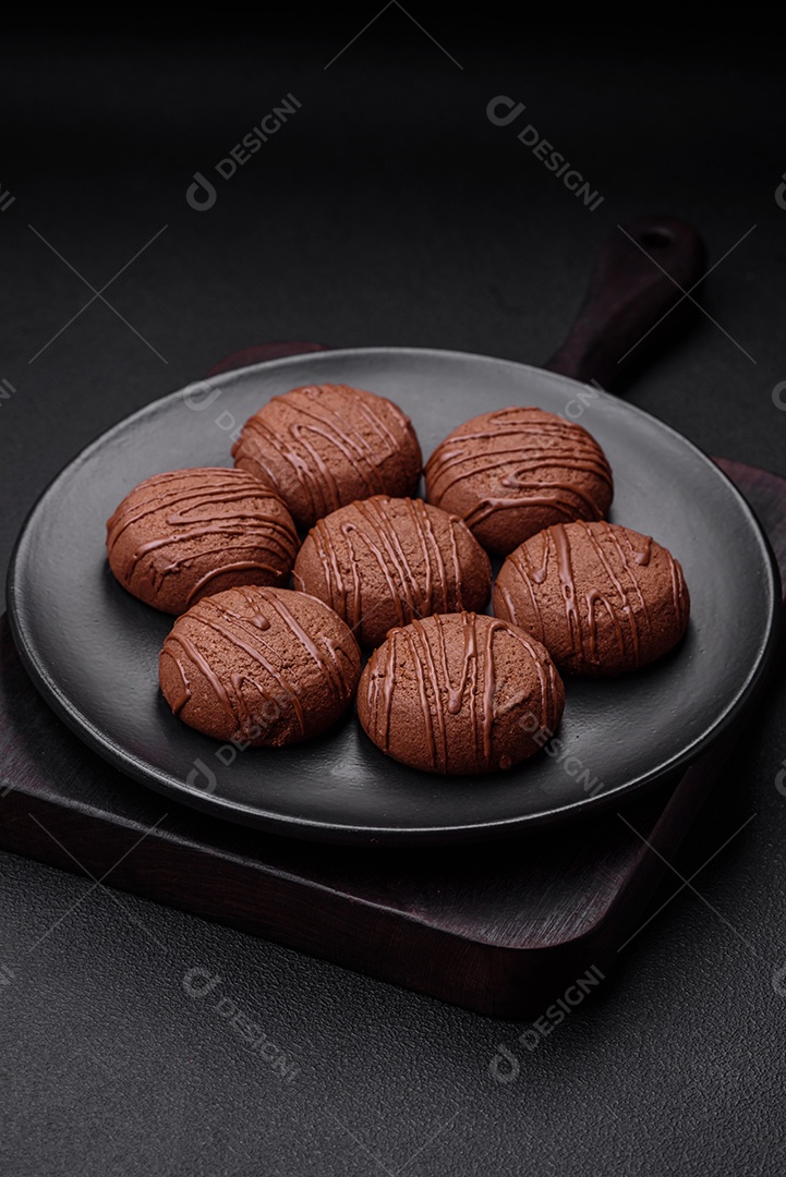 Deliciosos biscoitos de chocolate doce em uma placa de cerâmica preta sobre um fundo escuro de concreto