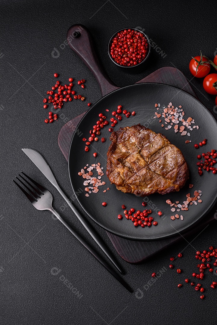 Delicioso bife suculento de porco ou bife grelhado com sal, especiarias e ervas sobre um fundo de concreto texturizado