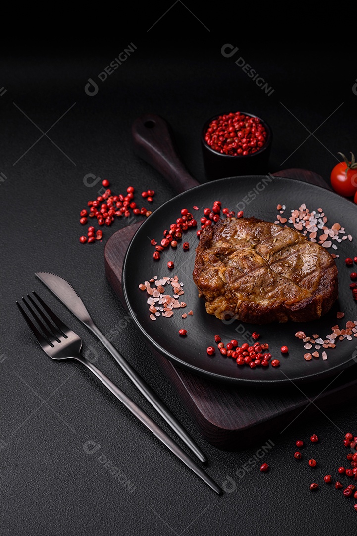 Delicioso bife suculento de porco ou bife grelhado com sal, especiarias e ervas sobre um fundo de concreto texturizado