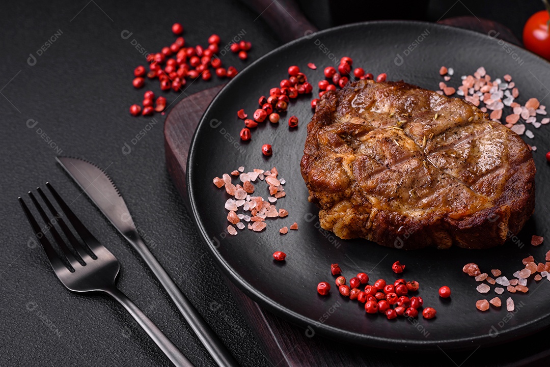 Delicioso bife suculento de porco ou bife grelhado com sal, especiarias e ervas sobre um fundo de concreto texturizado