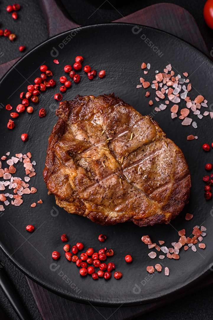 Delicioso bife suculento de porco ou bife grelhado com sal, especiarias e ervas sobre um fundo de concreto texturizado