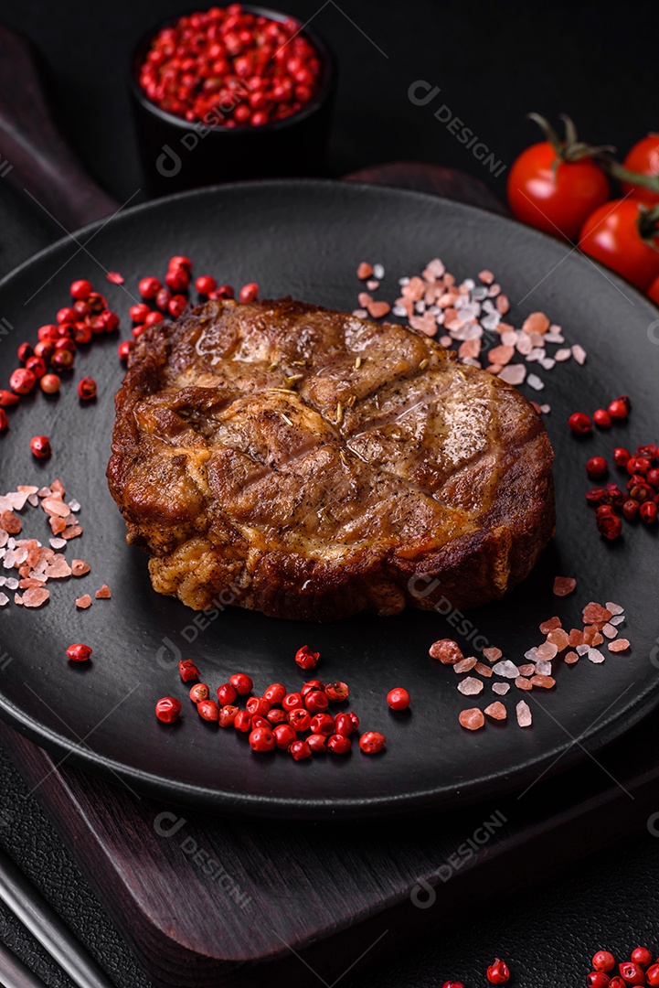 Delicioso bife suculento de porco ou bife grelhado com sal, especiarias e ervas sobre um fundo de concreto texturizado