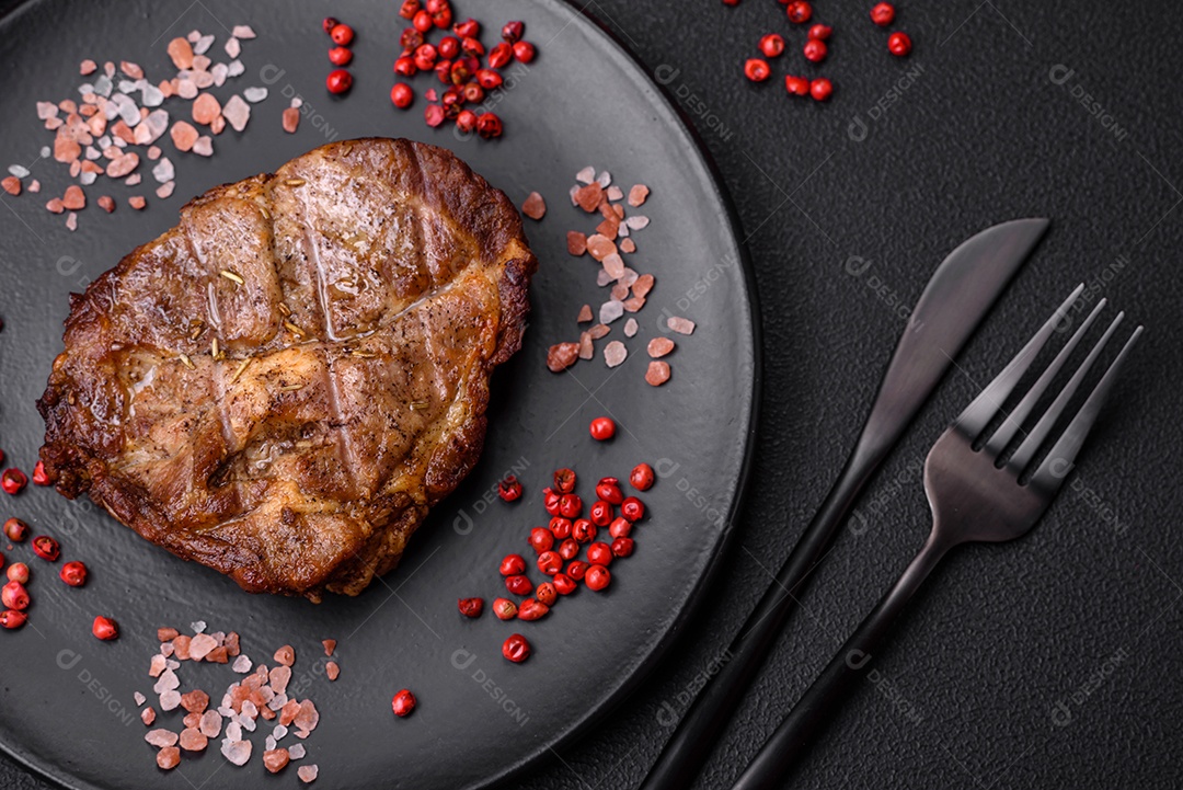 Delicioso bife suculento de porco ou bife grelhado com sal, especiarias e ervas sobre um fundo de concreto texturizado