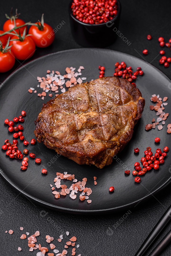 Delicioso bife suculento de porco ou bife grelhado com sal, especiarias e ervas sobre um fundo de concreto texturizado