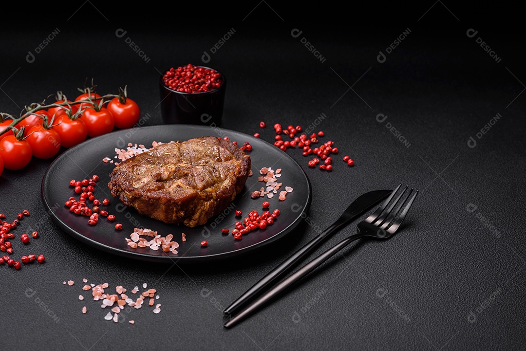 Delicioso bife suculento de porco ou bife grelhado com sal, especiarias e ervas sobre um fundo de concreto texturizado