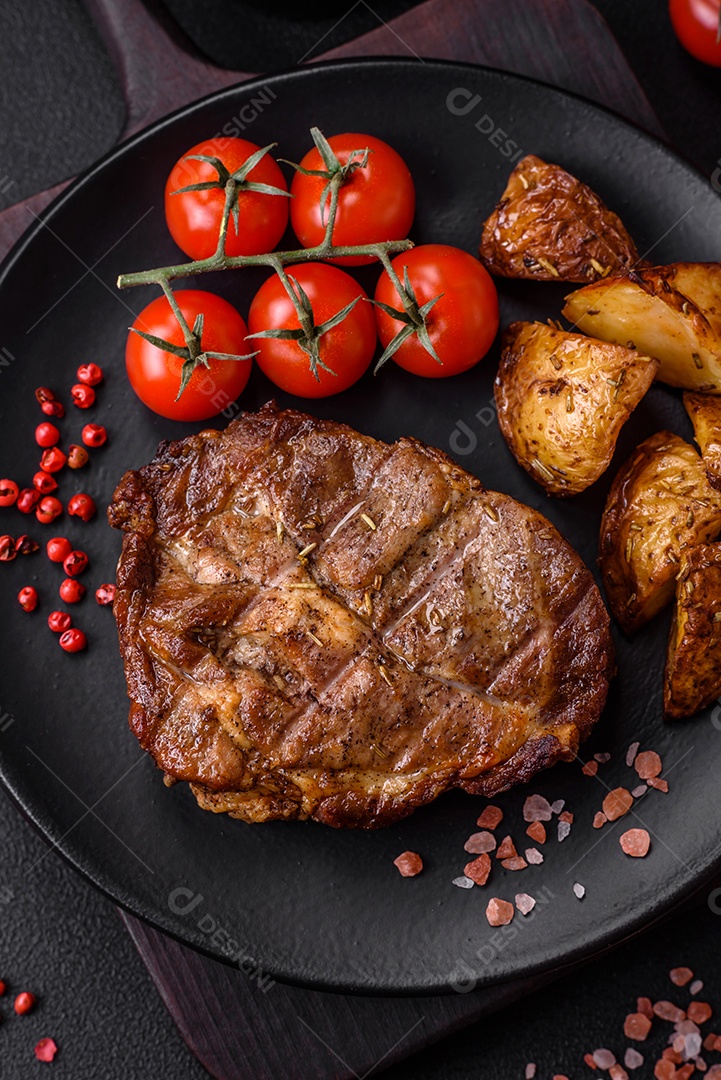 Delicioso bife suculento de porco ou bife grelhado com sal, especiarias e ervas sobre um fundo de concreto texturizado