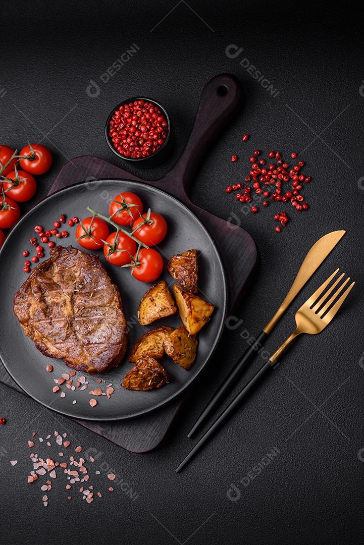 Delicioso bife com sal, especiarias e ervas em uma placa cerâmica sobre um fundo escuro de concreto