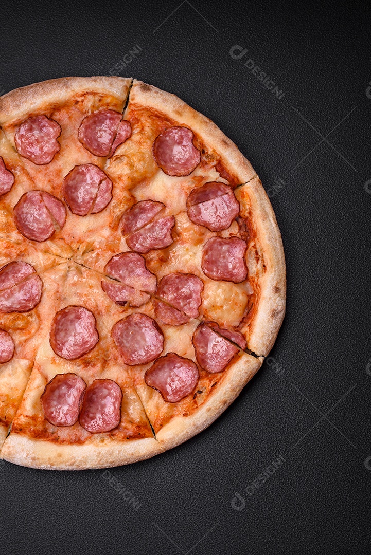 Saborosa pizza fresca com salame, queijo, tomate, especiarias e sal sobre um fundo escuro de concreto