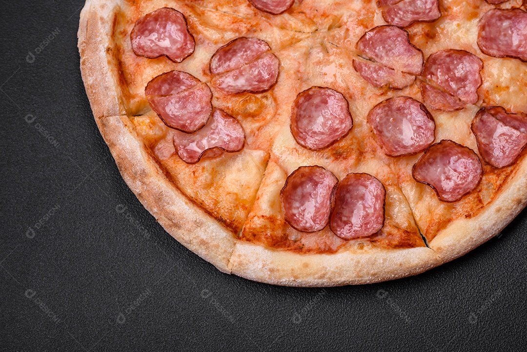 Saborosa pizza fresca com salame, queijo, tomate, especiarias e sal sobre um fundo escuro de concreto