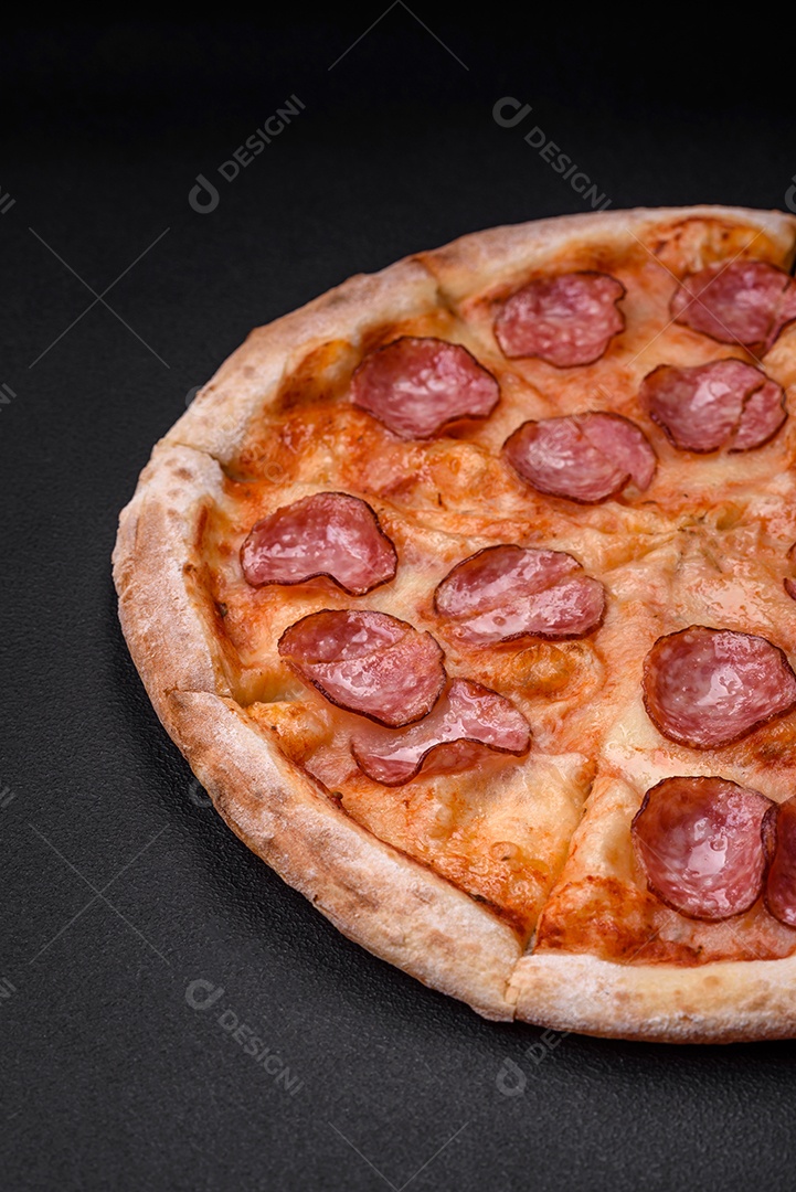 Saborosa pizza fresca com salame, queijo, tomate, especiarias e sal sobre um fundo escuro de concreto