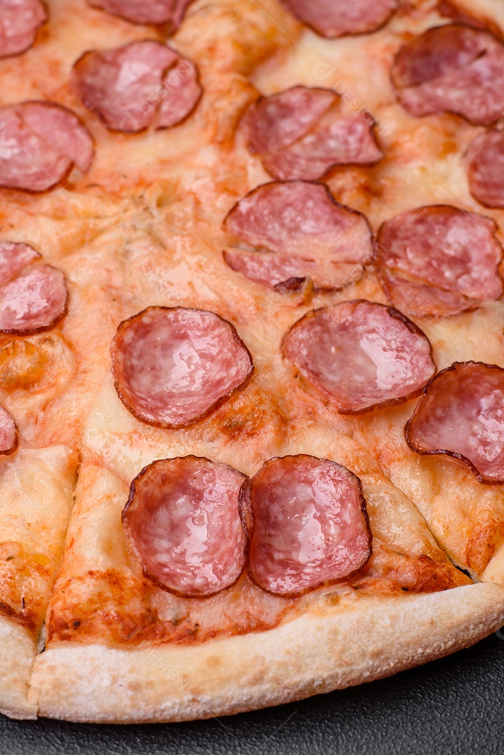 Pizza bávara com enchidos, tomates, queijo, sal e especiarias sobre um fundo escuro de concreto