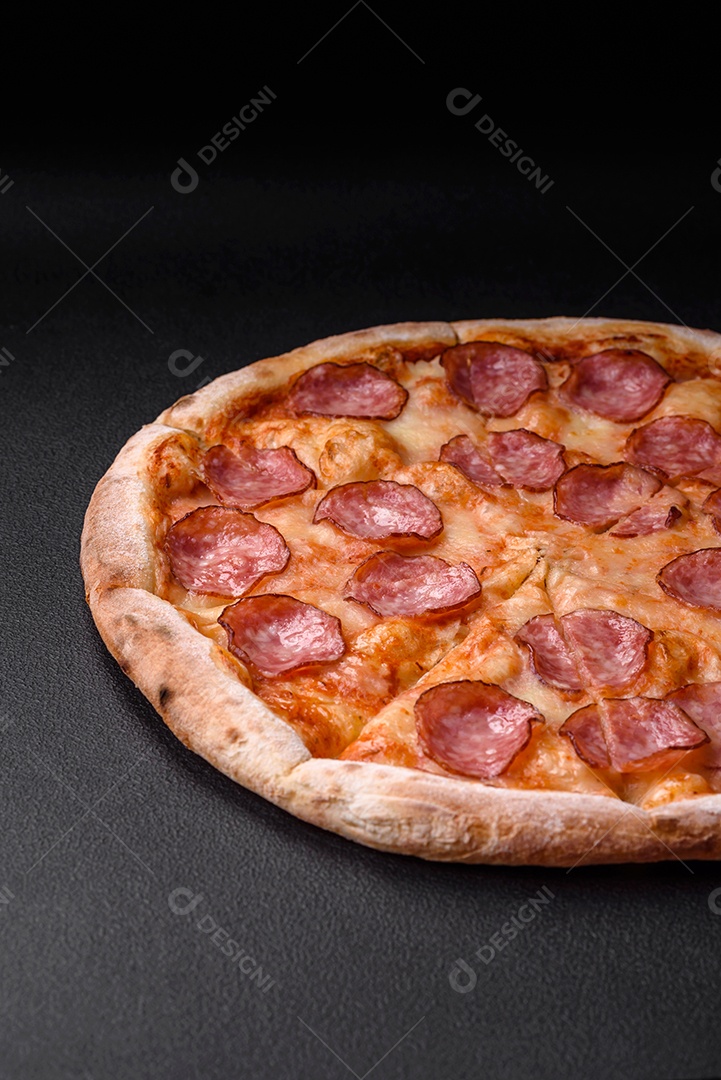 Saborosa pizza fresca com salame, queijo, tomate, especiarias e sal sobre um fundo escuro de concreto