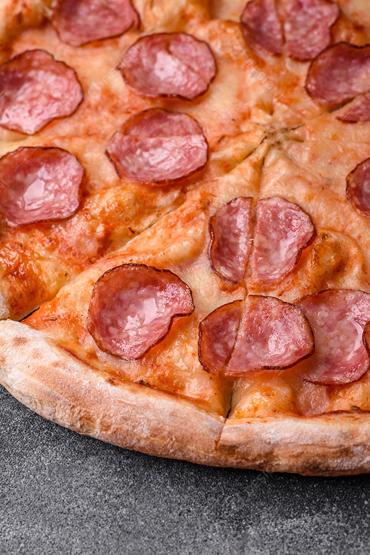 Saborosa pizza fresca com salame, queijo, tomate, especiarias e sal sobre um fundo escuro de concreto