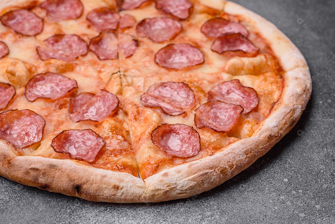 Saborosa pizza fresca com salame, queijo, tomate, especiarias e sal sobre um fundo escuro de concreto