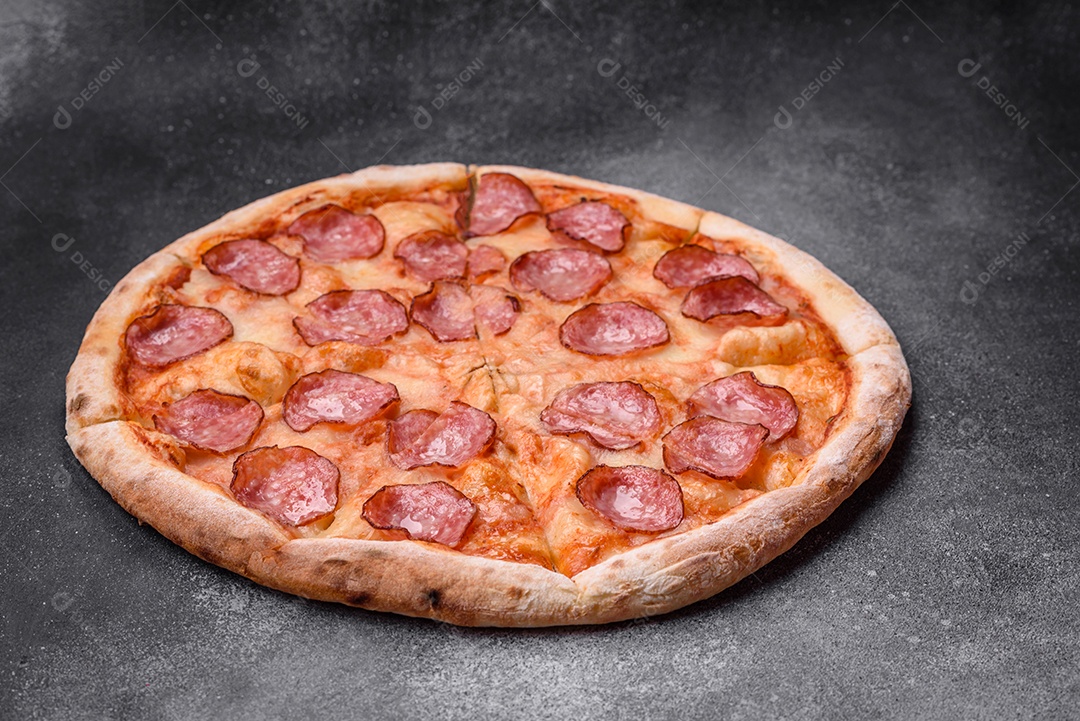 Saborosa pizza fresca com salame, queijo, tomate, especiarias e sal sobre um fundo escuro de concreto