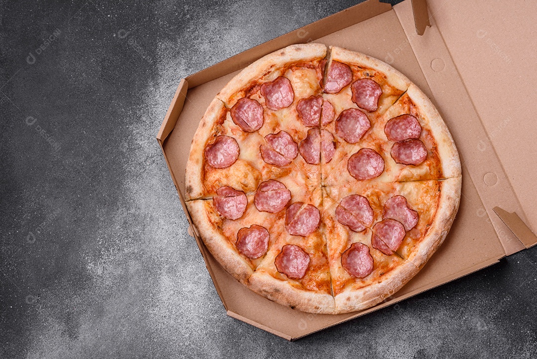 Saborosa pizza fresca com salame, queijo, tomate, especiarias e sal sobre um fundo escuro de concreto