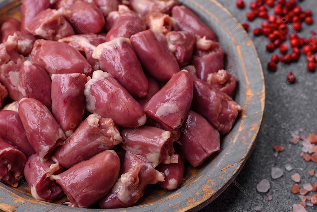 Corações crus de frango ou peru com sal, especiarias e ervas sobre um fundo de concreto texturizado