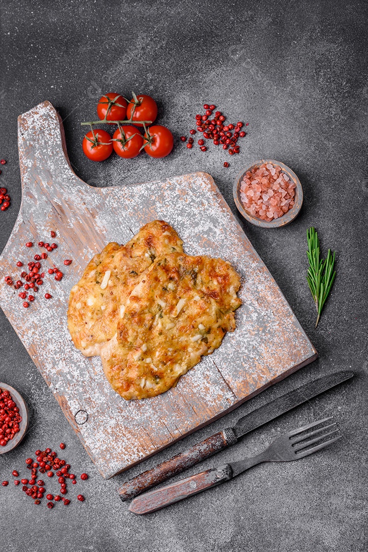 Delicioso peito de frango frito em massa com mostarda, sal, especiarias e queijo sobre fundo escuro de concreto