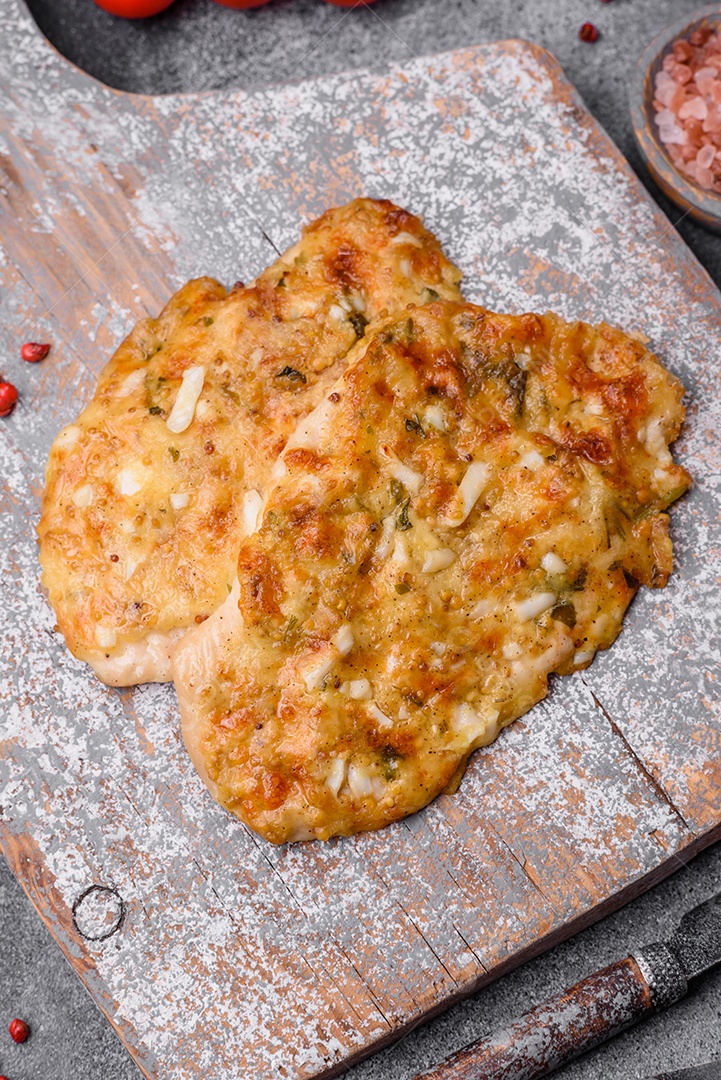 Delicioso peito de frango frito em massa com mostarda, sal, especiarias e queijo sobre fundo escuro de concreto