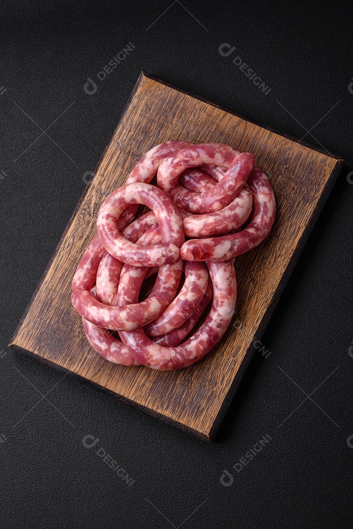 Salsichas cruas de porco ou vaca com sal, especiarias e ervas sobre um fundo escuro de concreto