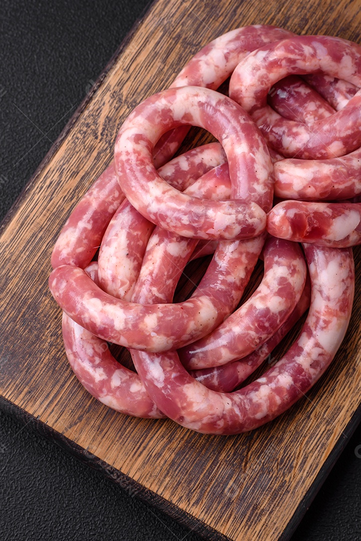 Salsichas cruas de porco ou vaca com sal, especiarias e ervas sobre um fundo escuro de concreto