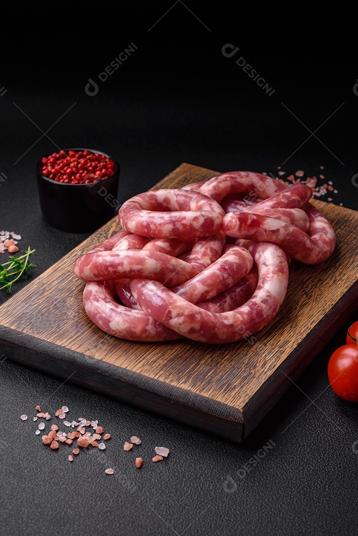 Salsichas cruas de porco ou vaca com sal, especiarias e ervas sobre um fundo escuro de concreto