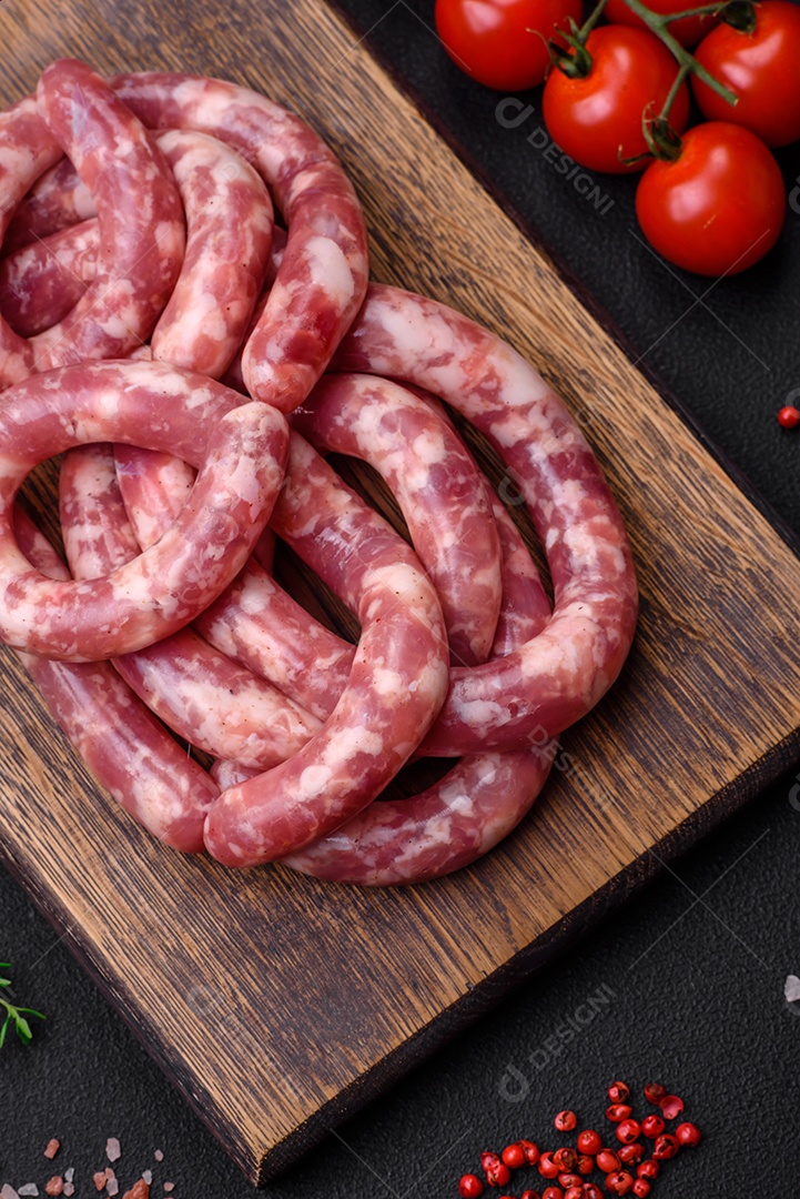 Salsichas cruas de porco ou vaca com sal, especiarias e ervas sobre um fundo escuro de concreto