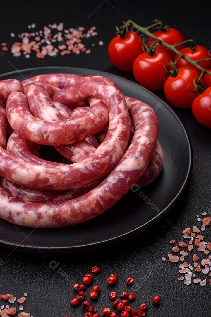 Salsichas cruas de porco ou vaca com sal, especiarias e ervas sobre um fundo escuro de concreto