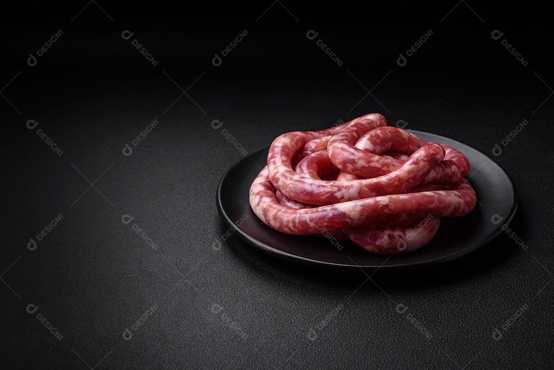 Salsichas cruas de porco ou vaca com sal, especiarias e ervas sobre um fundo escuro de concreto