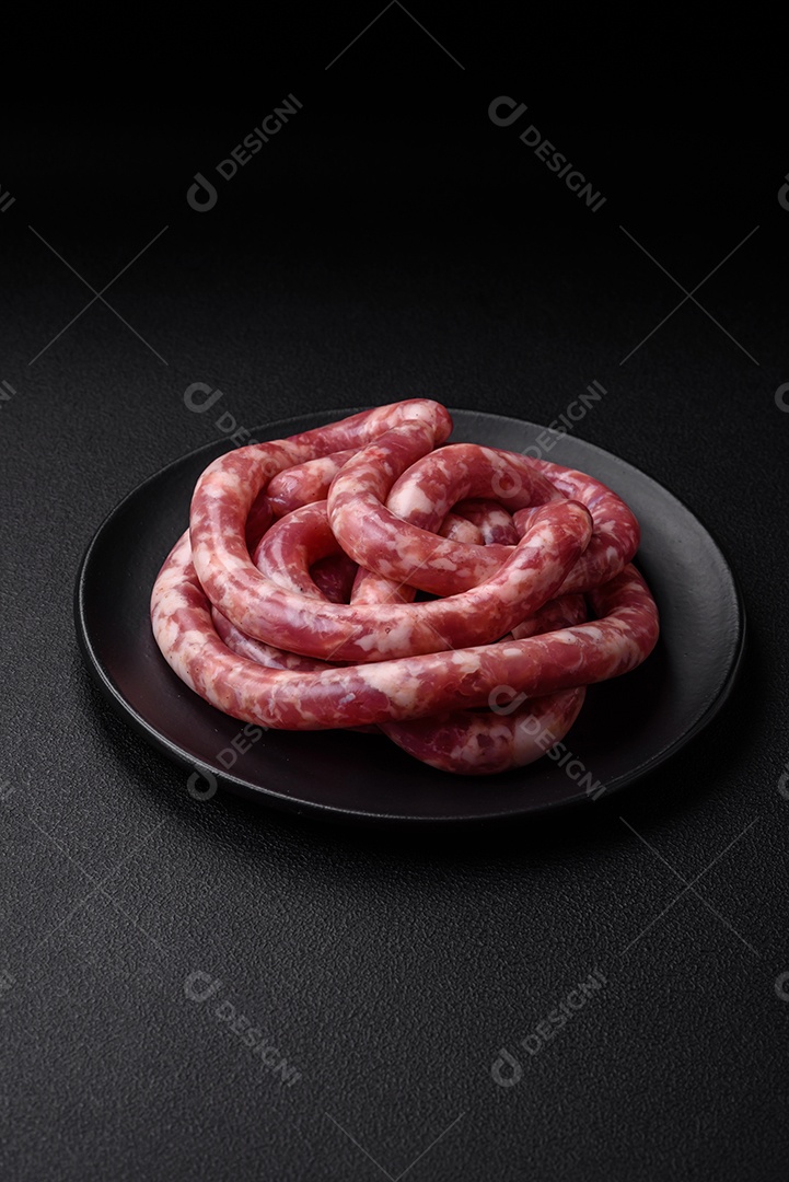 Salsichas cruas de porco ou vaca com sal, especiarias e ervas sobre um fundo escuro de concreto