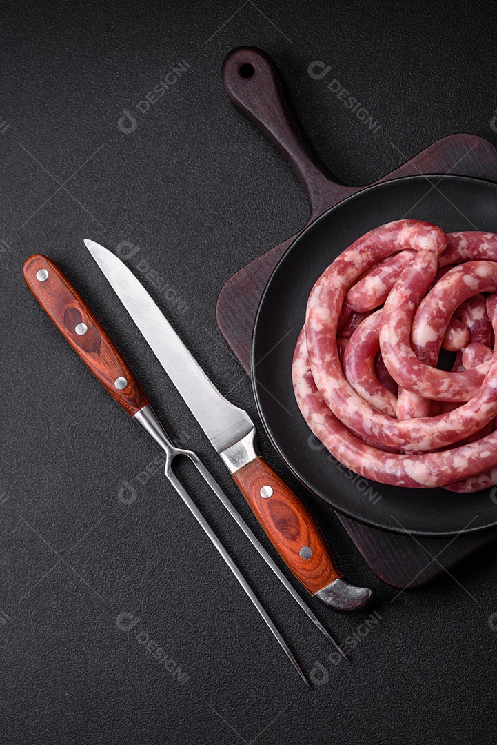 Salsichas cruas de porco ou vaca com sal, especiarias e ervas sobre um fundo escuro de concreto