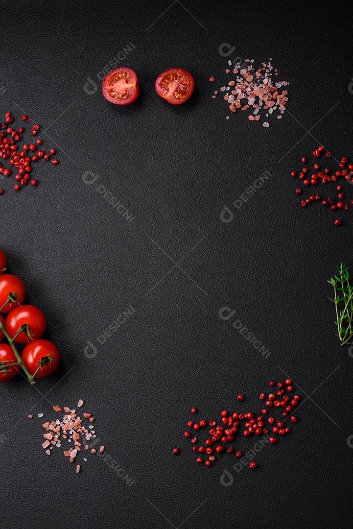 Ingredientes para cozinhar tomate cereja, sal, especiarias e ervas sobre um fundo escuro de concreto