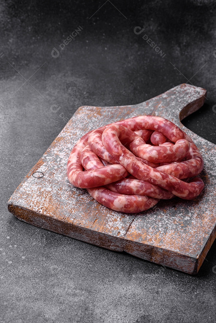 Salsichas cruas de porco ou vaca com sal, especiarias e ervas sobre um fundo escuro de concreto