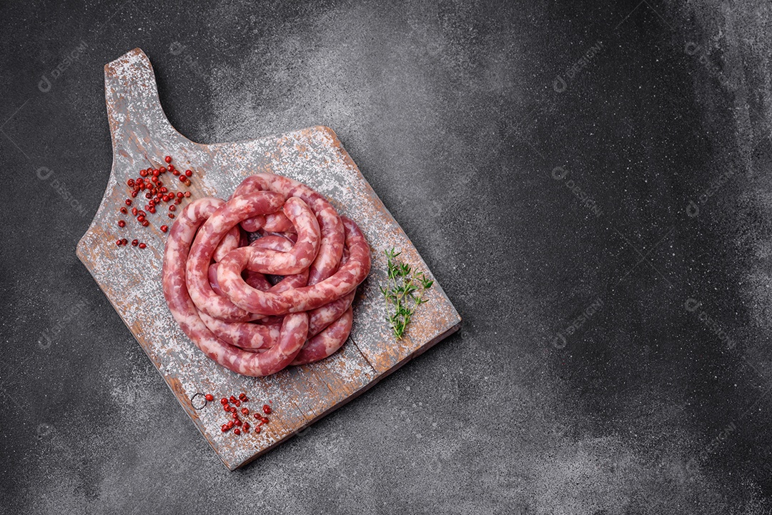 Salsichas cruas de porco ou vaca com sal, especiarias e ervas sobre um fundo escuro de concreto