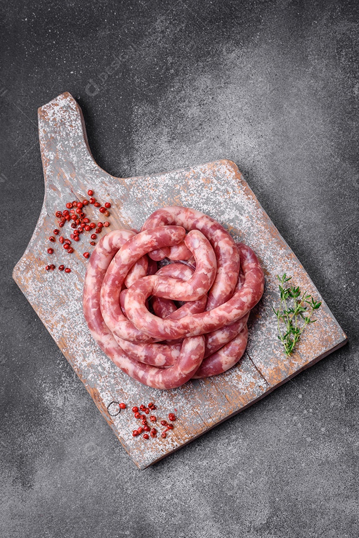 Salsichas cruas de porco ou vaca com sal, especiarias e ervas sobre um fundo escuro de concreto