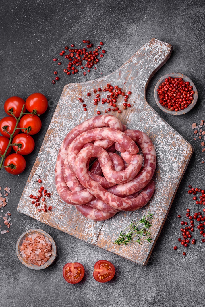 Salsichas cruas de porco ou vaca com sal, especiarias e ervas sobre um fundo escuro de concreto