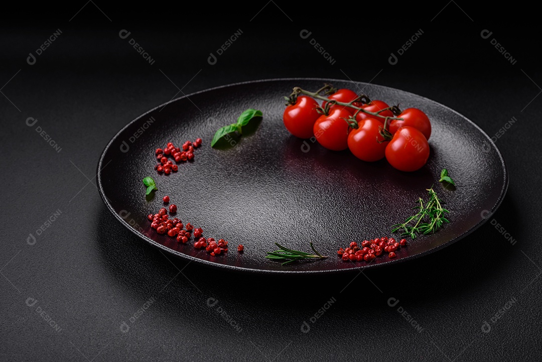 Ingredientes para cozinhar tomate cereja, sal, especiarias e ervas sobre um fundo escuro de concreto