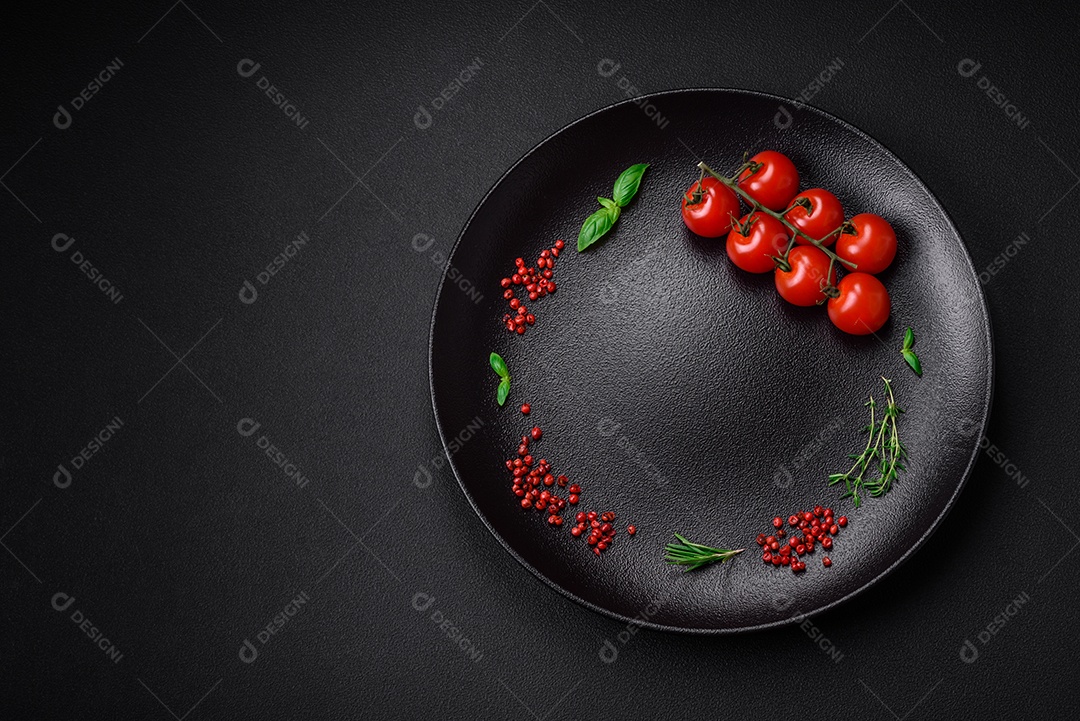 Ingredientes para cozinhar tomate cereja, sal, especiarias e ervas sobre um fundo escuro de concreto